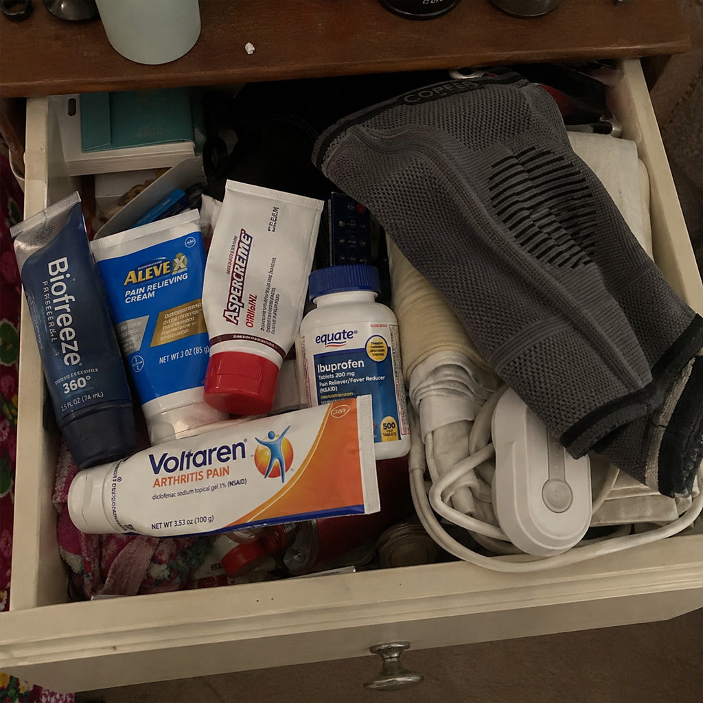 A drawer of half-used pain creams, a pill bottle, a rolled-up heating pad and a knee sleeve.
